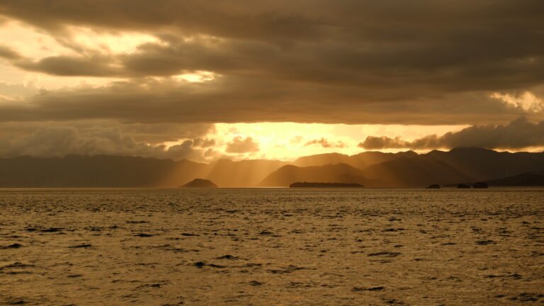 Golden sunset over the sea near Labuan Bajo with dramatic clouds and mountain silhouettes around Komodo National Park, Indonesia.