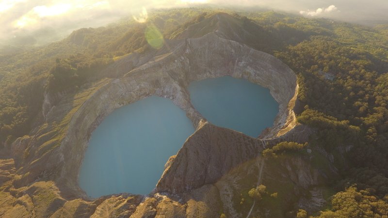 Pemandangan udara Danau Kelimutu dengan dua kawah berwarna biru yang dikelilingi perbukitan hijau saat matahari terbit.
