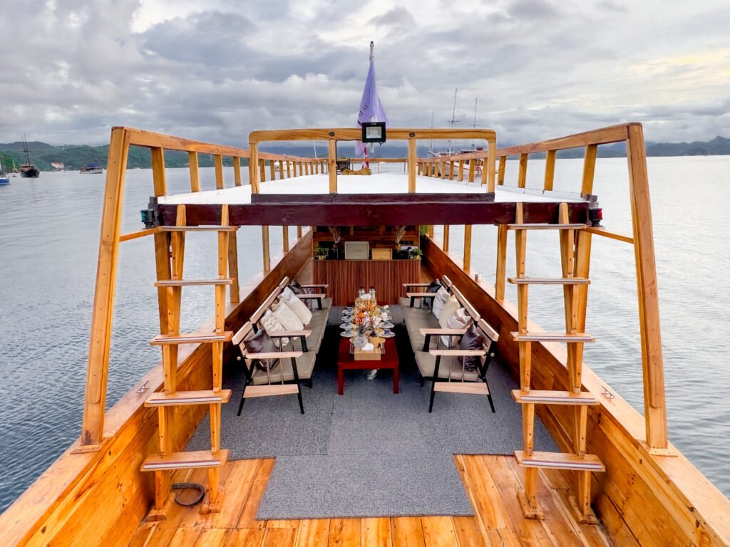 Luxury wooden phinisi boat deck with lounge seating and ocean view in Labuan Bajo under cloudy sky