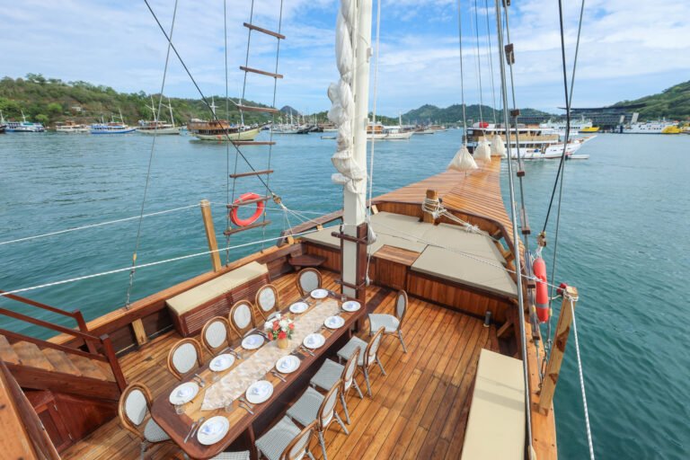Luxury phinisi boat deck in Labuan Bajo with outdoor dining setup, wooden interior, and ocean views during a Komodo sailing trip.