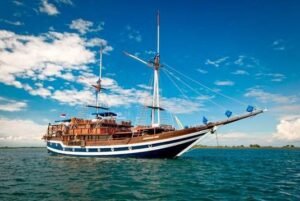 Kapal phinisi standard plus berlayar di perairan Raja Ampat dengan laut biru jernih dan cuaca cerah