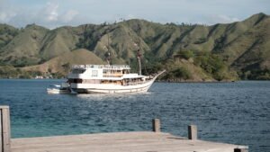 Kapal phinisi berlayar di perairan Labuan Bajo dengan latar perbukitan, ilustrasi perjalanan wisata dan checklist Labuan Bajo sebelum trip Komodo