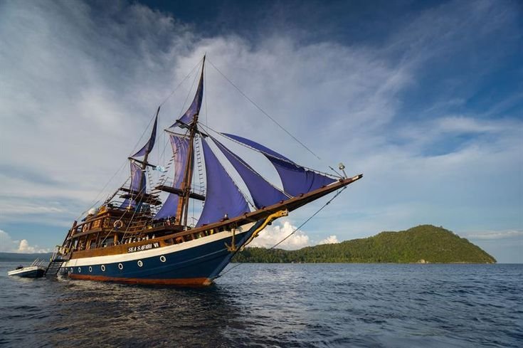 Phinisi liveaboard sailing in the waters of Raja Ampat with a tropical island backdrop and calm sea