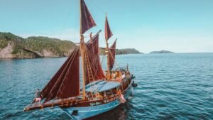 Kapal phinisi berlayar di perairan Raja Ampat dengan layar terkembang dan latar pulau tropis yang indah-visit labuan bajo komodo