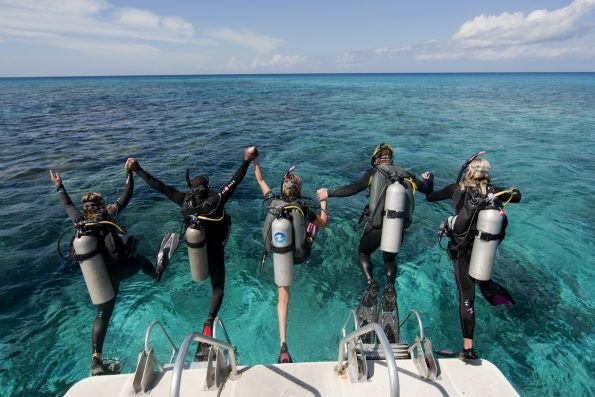 Group of scuba divers jumping into clear blue water in Labuan Bajo, preparing for a diving adventure in Komodo National Park.