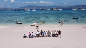 Group of tourists enjoying a beautiful beach day in Komodo National Park with crystal-clear turquoise water, tropical island scenery, and luxury phinisi boats during a Labuan Bajo island hopping tour — Visit Labuan Bajo Komodo.