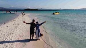 Romantic couple enjoying a private Komodo sailing trip on a pristine sandbank with turquoise water in Labuan Bajo, luxury honeymoon experience in Komodo National Park.