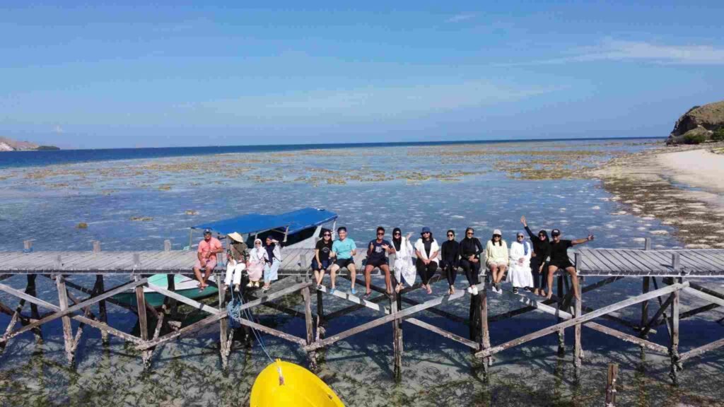 Group travelers enjoying a private Komodo island tour on a traditional wooden pier surrounded by crystal-clear turquoise water and beautiful tropical scenery in Labuan Bajo, Indonesia. This unforgettable Komodo National Park experience captures the essence of slow travel, island hopping, luxury sailing adventures, and authentic moments with friends and family during a private phinisi cruise.