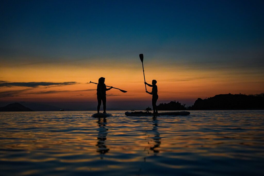 Sunset Labuan Bajo dengan aktivitas paddle board di laut tenang, wisata seru bersama visit labuan bajo”