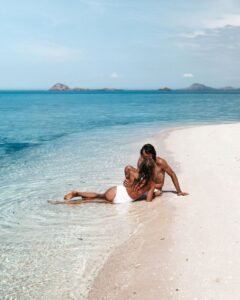 Romantic couple relaxing on a white sand beach in Komodo Islands with crystal-clear turquoise water and tropical island views in Labuan Bajo.