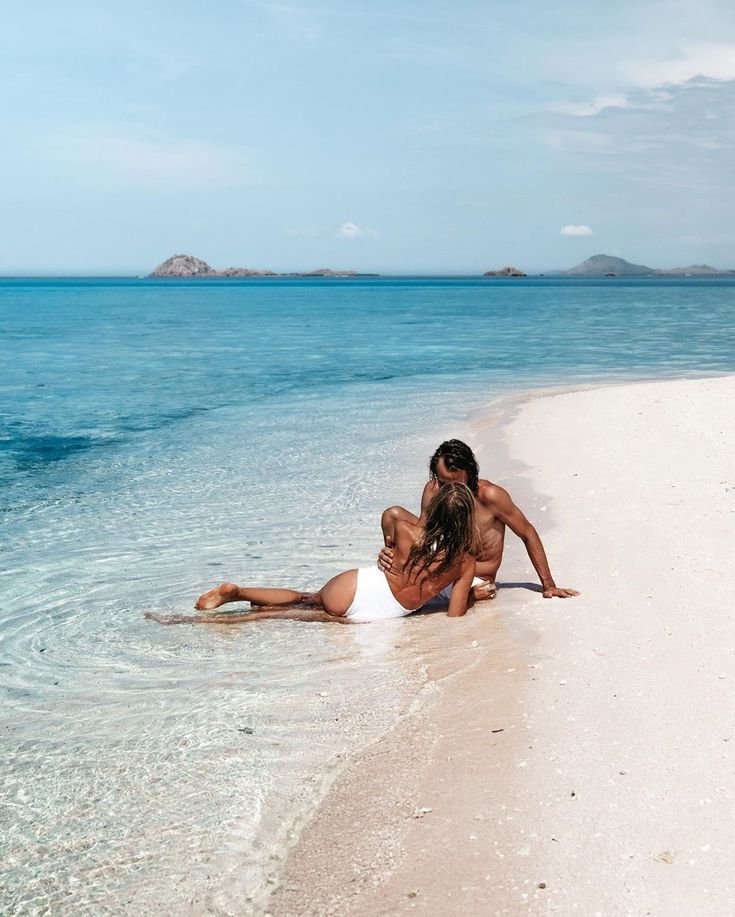 Romantic couple relaxing on a white sand beach in Komodo Islands with crystal-clear turquoise water and tropical island views in Labuan Bajo.