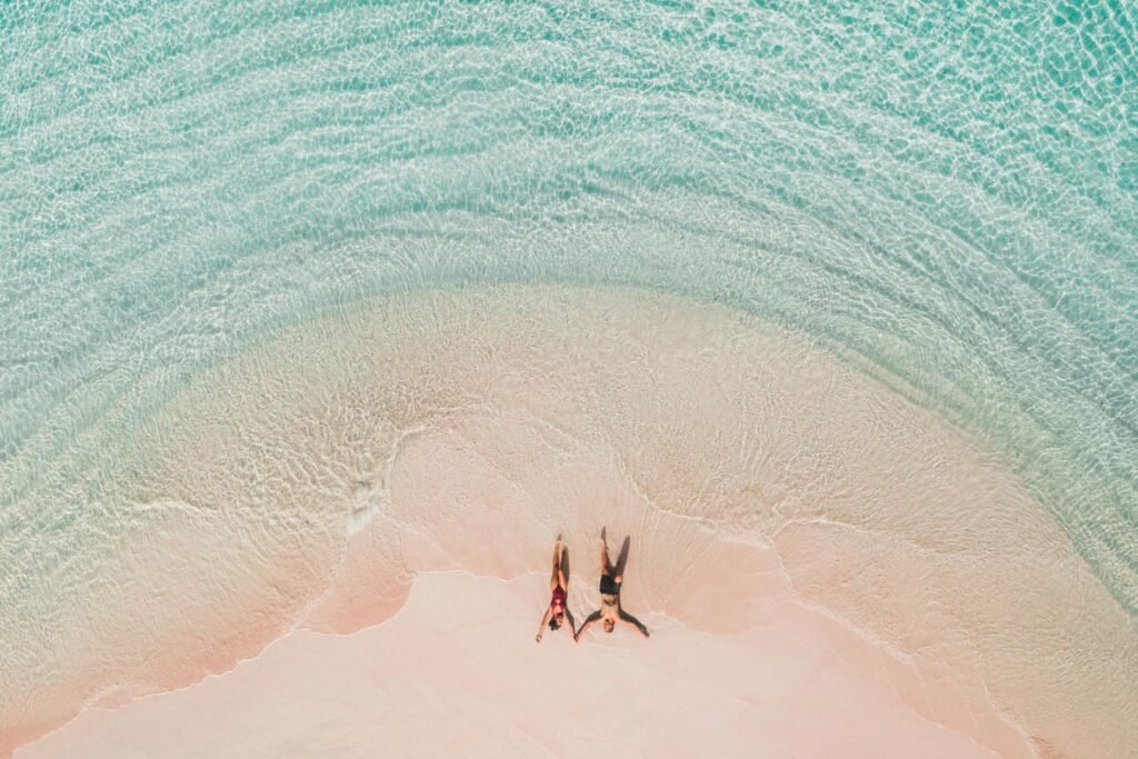 Beach couple relaxing on pink sand beach with crystal-clear turquoise water in Komodo National Park Indonesia