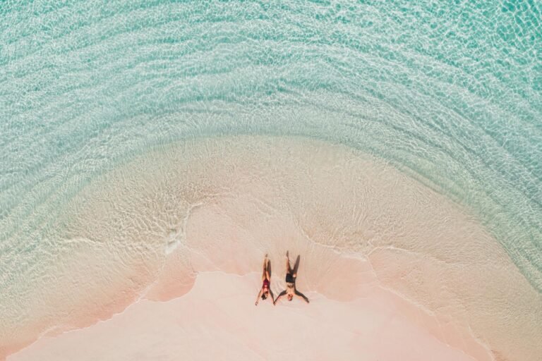 Beach couple relaxing on pink sand beach with crystal-clear turquoise water in Komodo National Park Indonesia