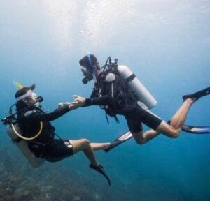 Couple scuba diving during PADI certification training in Komodo, Labuan Bajo, exploring clear blue waters and underwater adventure together. Fokus Keywords: