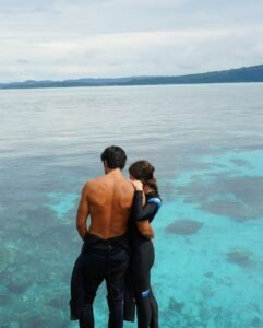 Romantic couple wearing diving suits overlooking crystal-clear turquoise waters during a luxury Komodo sailing trip near Labuan Bajo, Indonesia.