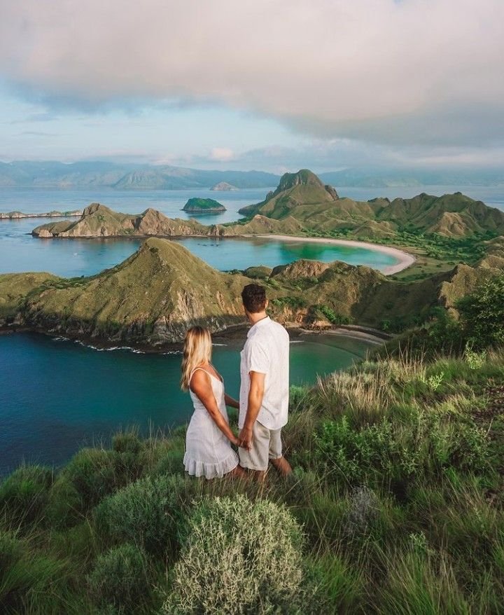 Couple enjoying the breathtaking Padar Island viewpoint overlooking turquoise bays and rolling hills in Komodo National Park, Indonesia.