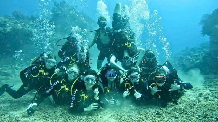 Group of beginner scuba divers exploring the vibrant underwater world of Komodo National Park during a Discover Scuba Diving experience with Visit Labuan Bajo Komodo, surrounded by coral reefs and crystal-clear blue waters.