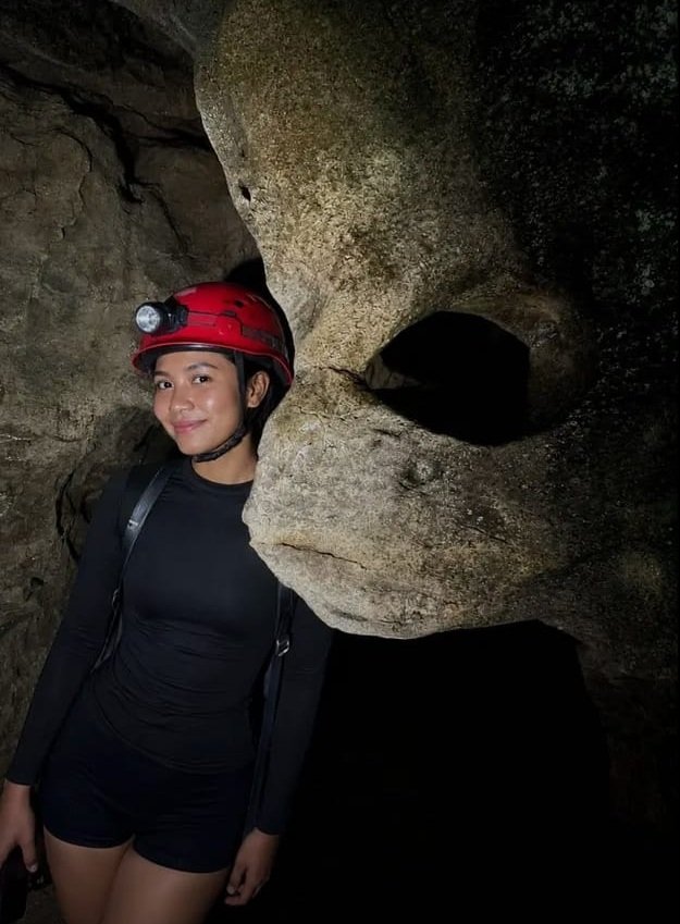 Explorer posing beside a skull-shaped rock formation inside Sampang Ngalak Cave, a hidden cave adventure near Labuan Bajo, Flores with Visit Labuan Bajo.